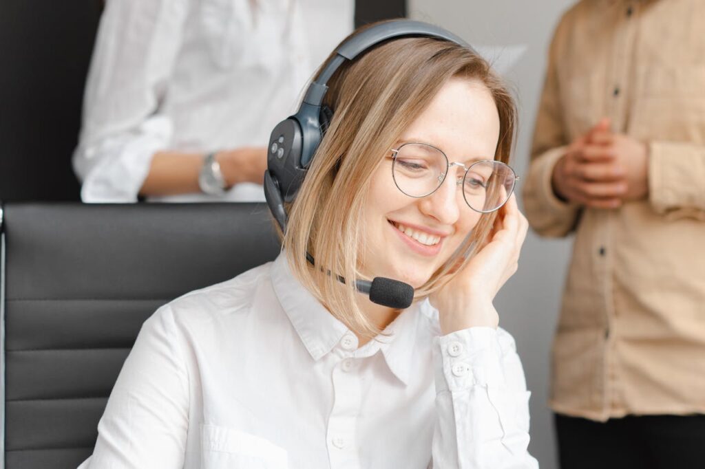 pexels-photo-7682204 A cheerful woman working at a call center, wearing a headset and glasses, providing excellent customer support.