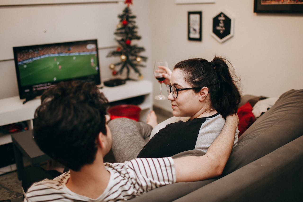 A couple enjoying a cozy evening on the sofa, watching TV with holiday decor in the background.